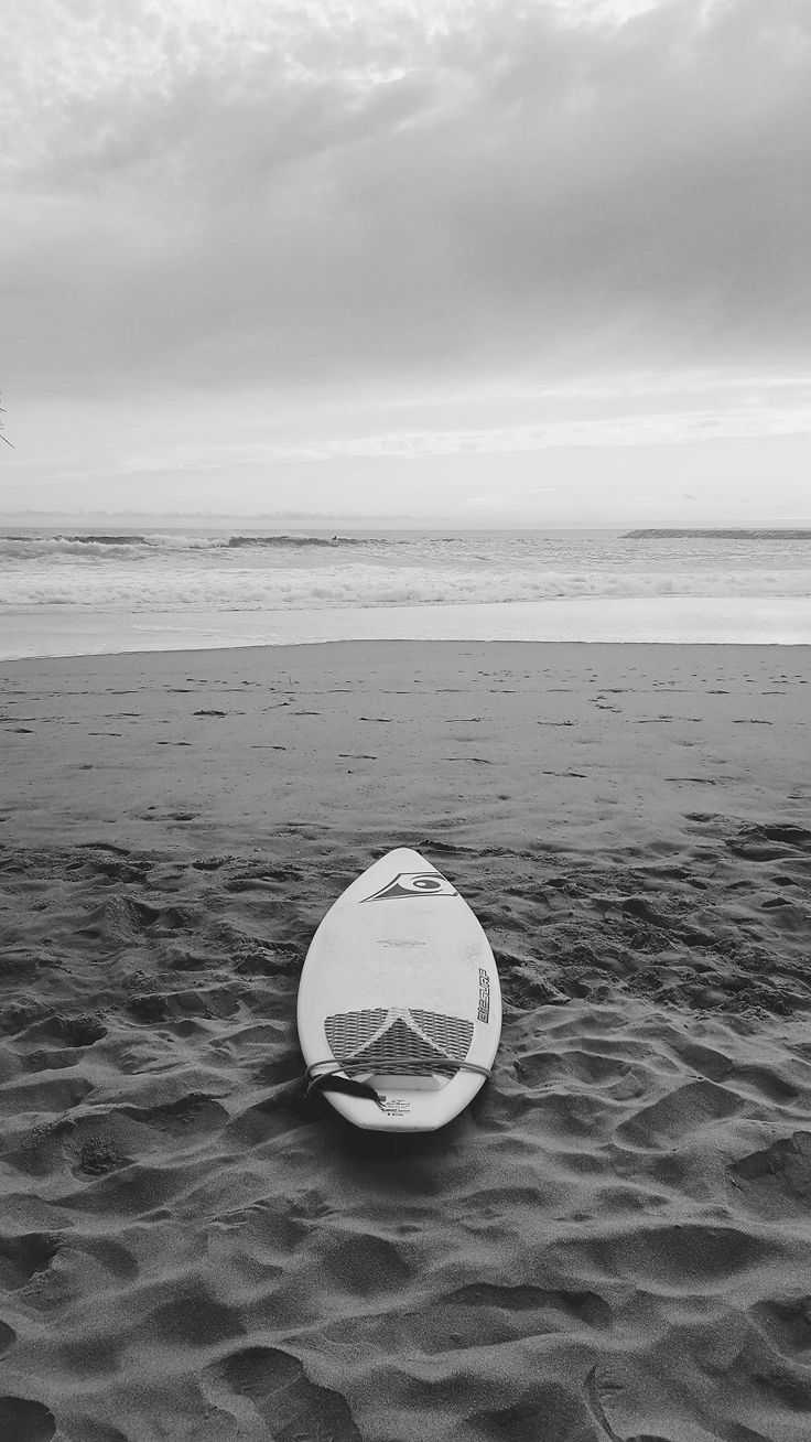 a surfboard sitting on top of a sandy beach next to the ocean in black and white