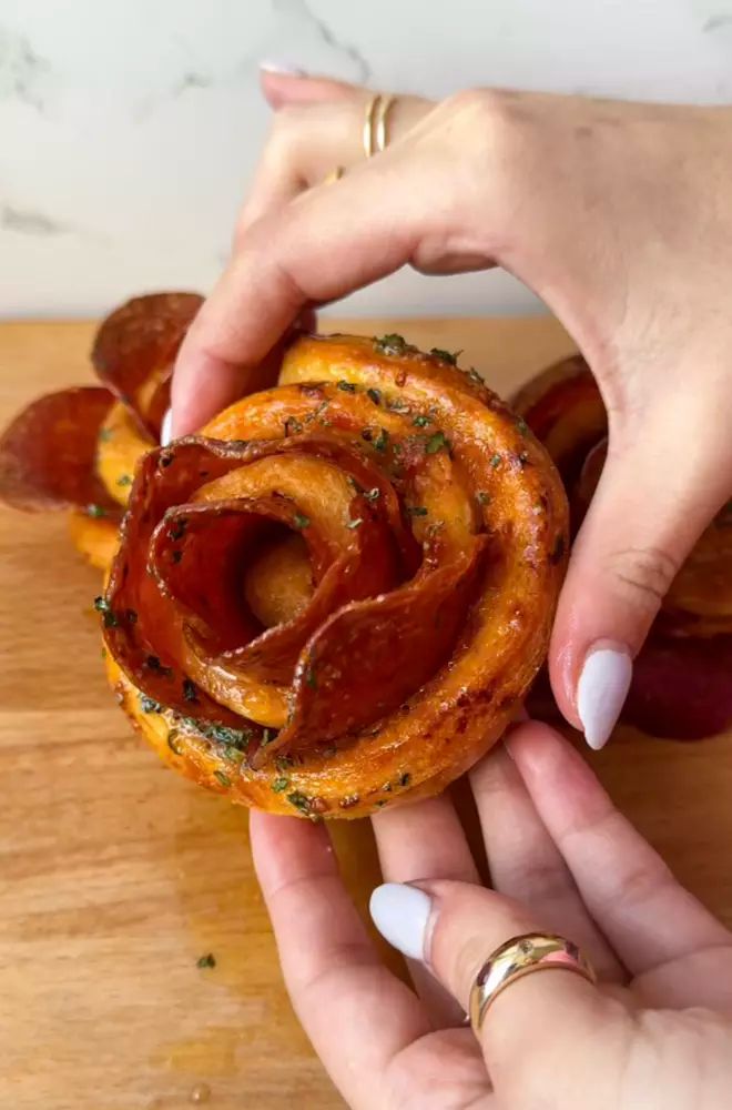 two hands holding a pastry that looks like a spiral onion roll with bacon on top