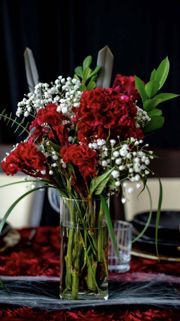 a vase filled with red and white flowers on top of a dining room tablecloth