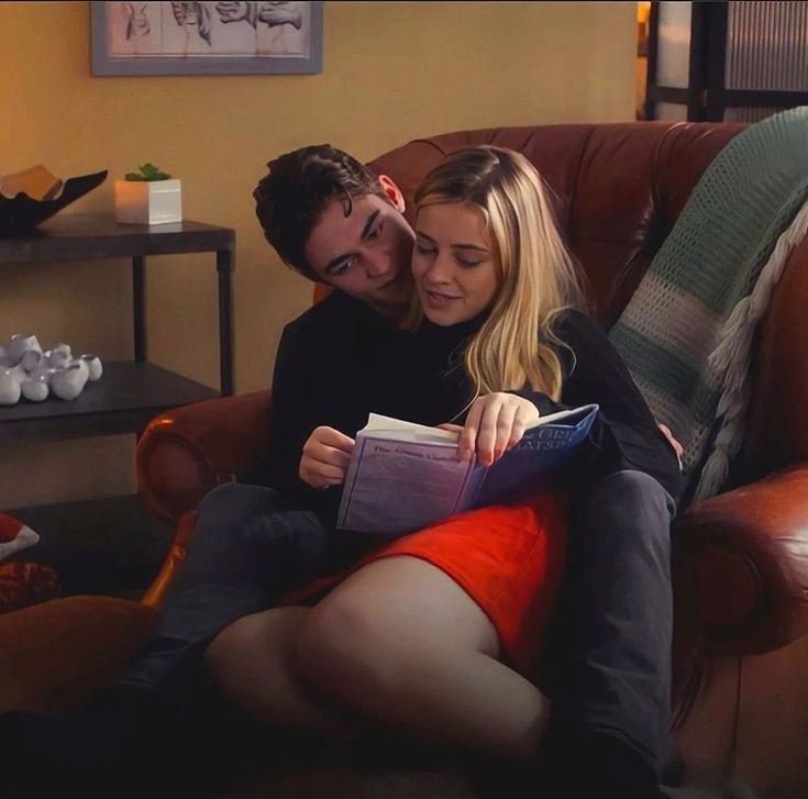 a man and woman sitting on a couch looking at a book