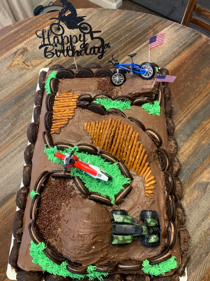 a birthday cake that is shaped like a dirt bike track with green and brown frosting