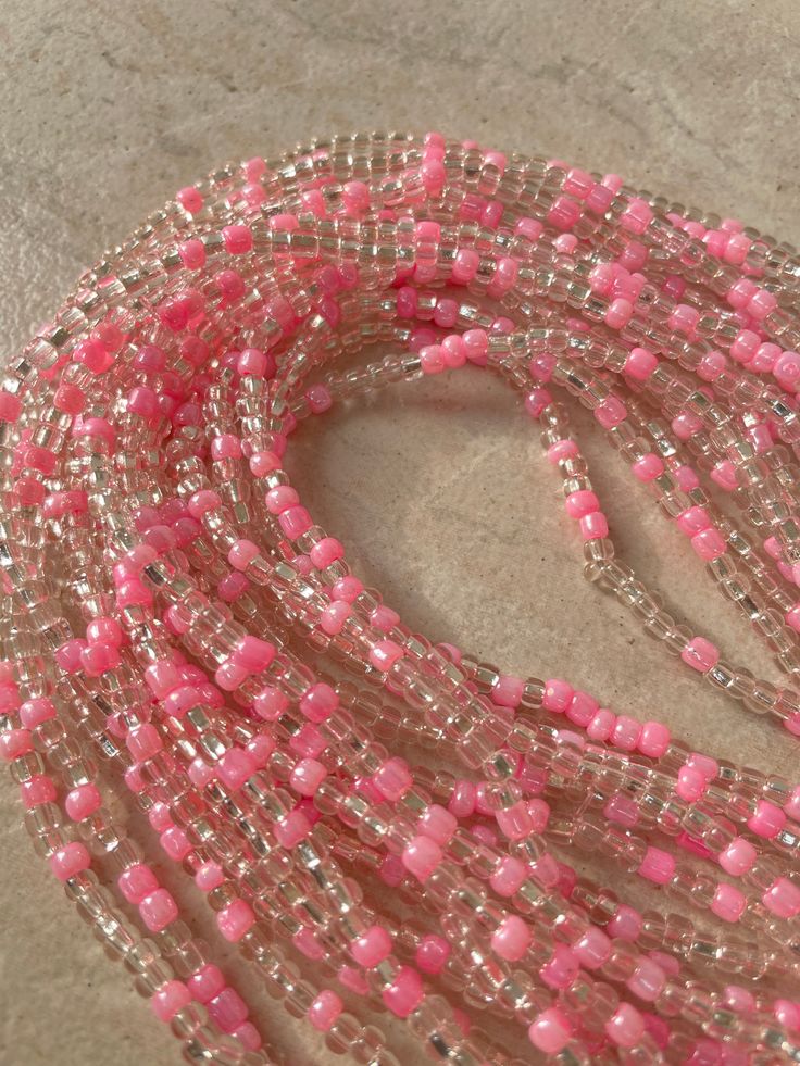 Elastic Waist Bead "Diawala" features strands of clear and silvery glass seed beads, elegantly adorned with delicate baby pink seed bead accents. Elevate your style with the timeless beauty of this harmonious blend, offering a touch of sophistication and gentle femininity. 💫 Clear and Silvery Radiance: This elastic waist bead gleams with clarity, adorned with clear and silvery glass seed beads that reflect a subtle, luminous radiance. The combination creates a versatile backdrop, allowing the a Pink Tiny Beads Necklace For Jewelry Making, Pink Beaded Necklaces For Festivals, Pink Tiny Beaded Bracelets For Party, Pink Round Beaded Jewelry For Festivals, Pink Bohemian Tiny Beaded Necklace, Elegant Pink Beaded Necklace With Tiny Beads, Pink Spacer Beaded Necklace For Festivals, Pink Spacer Beads Necklace For Festival, Pink Spacer Bead Necklaces For Festivals