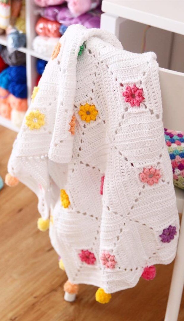 a white crocheted blanket hanging from a rack next to a chair and rug