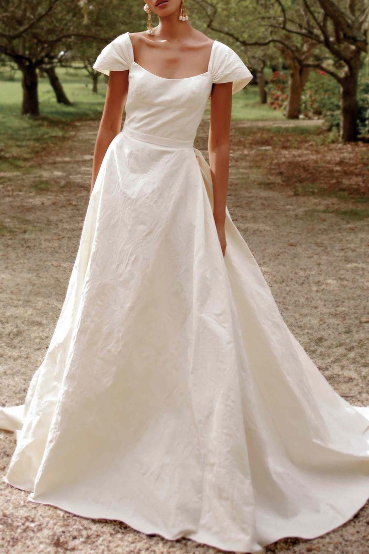 a woman in a white wedding dress posing for the camera with trees in the background