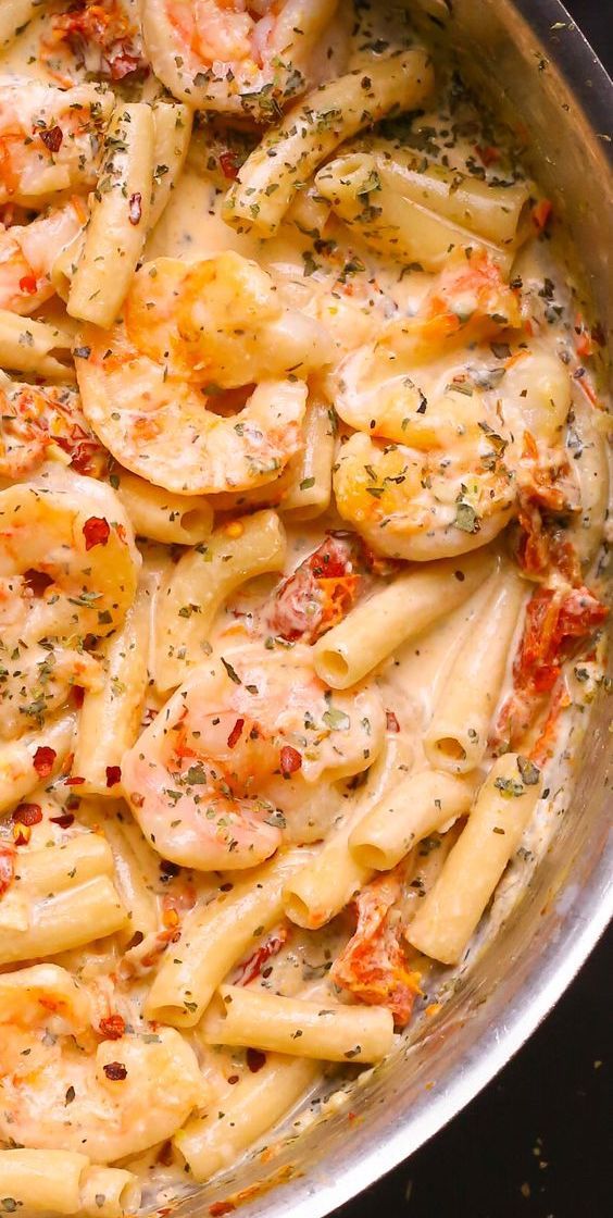 a pan filled with pasta and shrimp covered in seasoning sprinkled on top