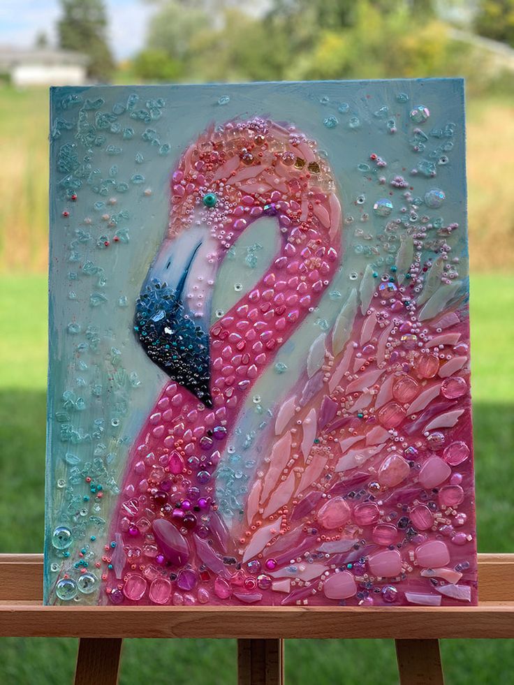 a pink flamingo painting sitting on top of a easel in front of a field