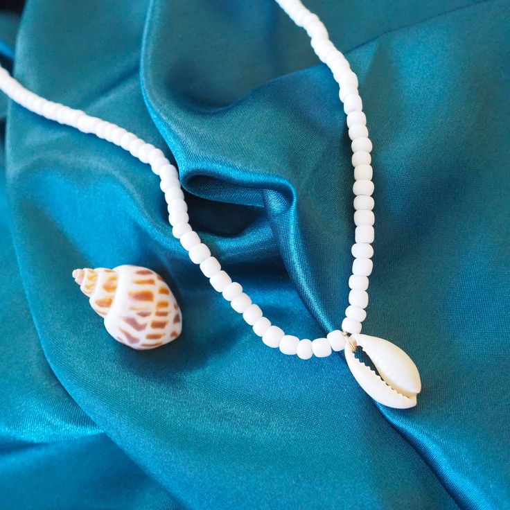 Introducing the Po'olenalena Layers Necklace – a charming duo inspired by the tranquil beauty of Po'olenalena Beach! This delightful layered necklace set brings a touch of the Hawaiian shores to your style. Wear them together for a stunning layered look or separately for a subtle island vibe. The first necklace features delicate white beads with a beautiful cowry shell centerpiece, perfect for adding a touch of elegance to your beachy ensemble. The second necklace is a string of enchanting cowry shells, capturing the essence of the ocean's treasures. Handcrafted with care, the Po'olenalena Layers Necklace is your go-to accessory for any sun-soaked adventure or tropical getaway. Embrace the spirit of the islands and let your inner beach lover shine! Seashells: real cowry White beads with lo Elegant White Shell Necklace For Summer, White Shell Necklace With Clavicle Chain, White Shell Charm Necklace As Gift, White Shell Charm Necklace Gift, White Shell Charm Necklace For Gift, Elegant White Strand Jewelry, White Shell-shaped Necklace For A Gift, White Shell-shaped Necklace For Gift, White Shell Charm Necklaces