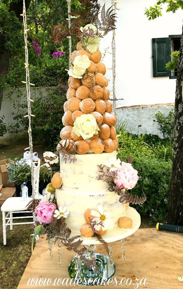 a tall white cake sitting on top of a wooden table in front of a tree