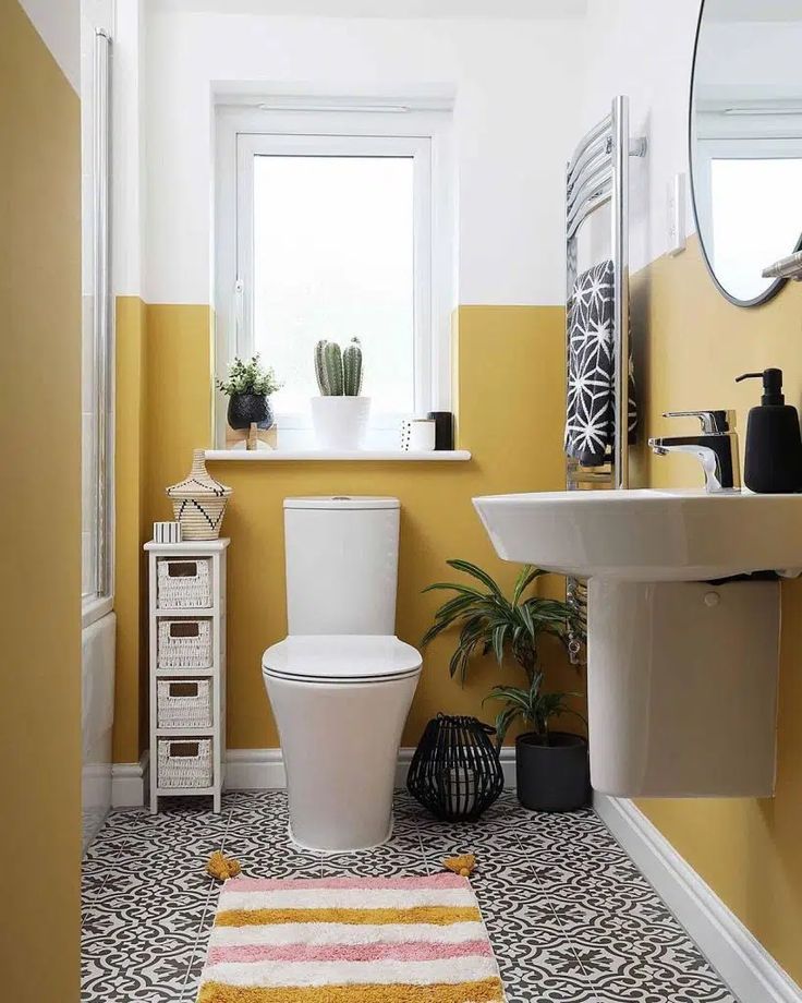 a white toilet sitting next to a sink in a bathroom under a window with yellow walls