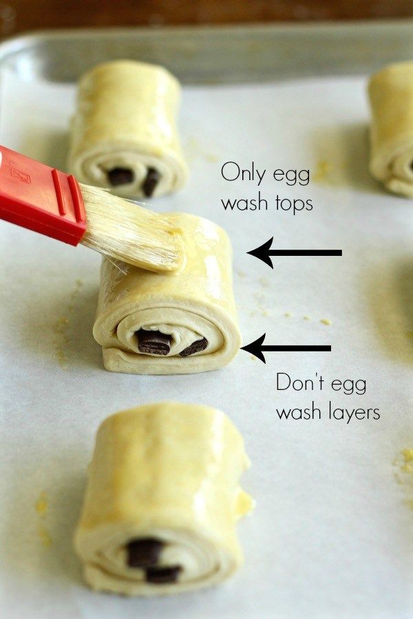 rolled up food items on a baking sheet with an egg wash top and red spatula