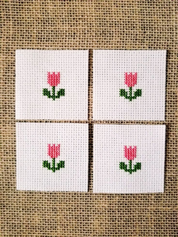 four cross stitch coasters with pink flowers on them