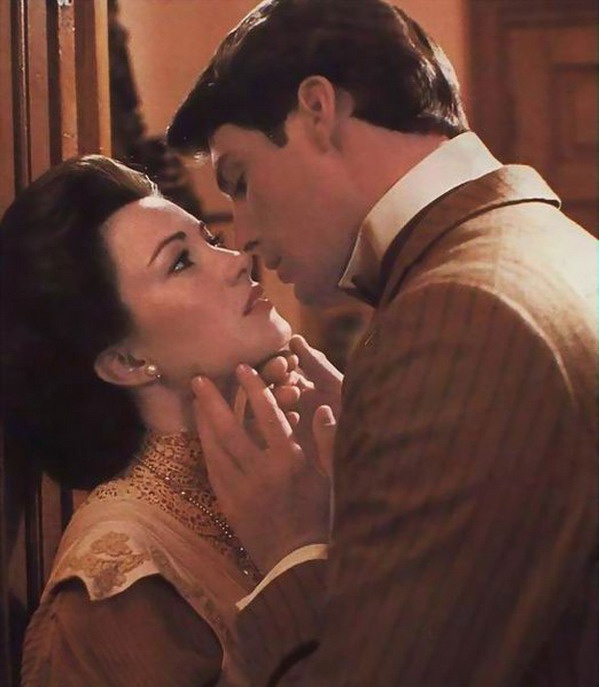 the man and woman are kissing each other in front of an open door with their faces close together