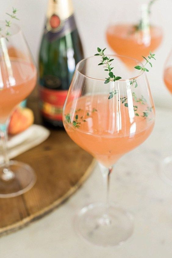 three glasses filled with pink wine and garnished with green sprigs on a wooden tray