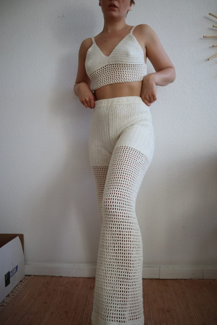 a woman in white pants and crop top posing for the camera with her hands on her hips