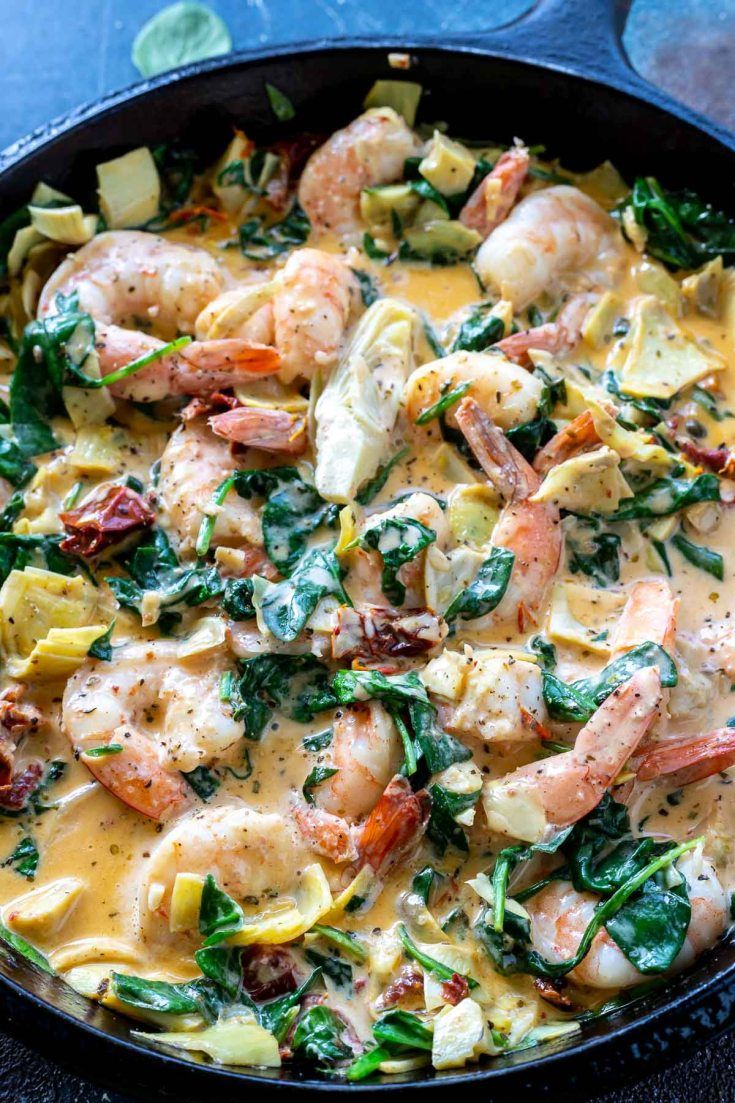 a skillet with shrimp, spinach and cheese in it on a blue surface