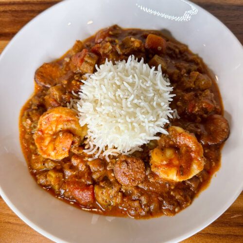 a white bowl filled with food and rice on top of a wooden table next to a spoon