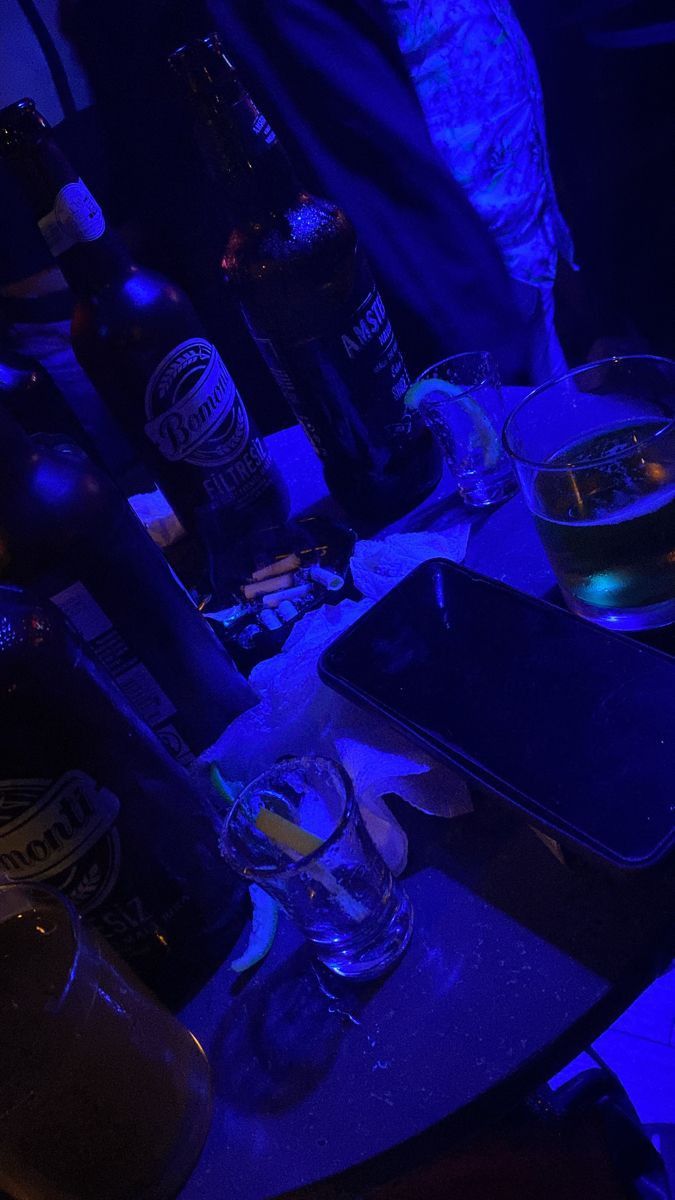 a table topped with bottles and glasses next to a cell phone on top of a wooden table