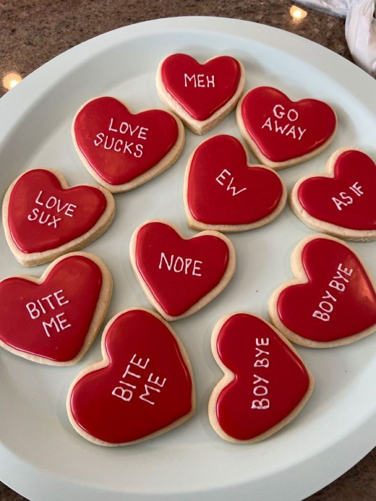 heart - shaped cookies with words written on them are arranged on a white platter