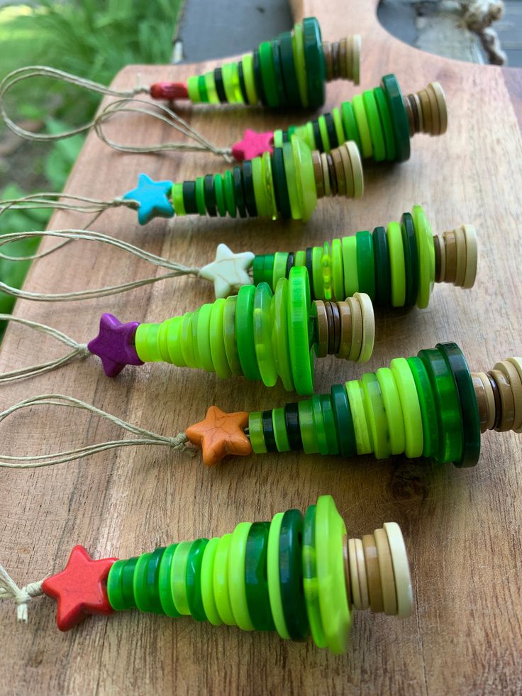 colorful wooden christmas tree ornaments are lined up on a cutting board with string and star pins