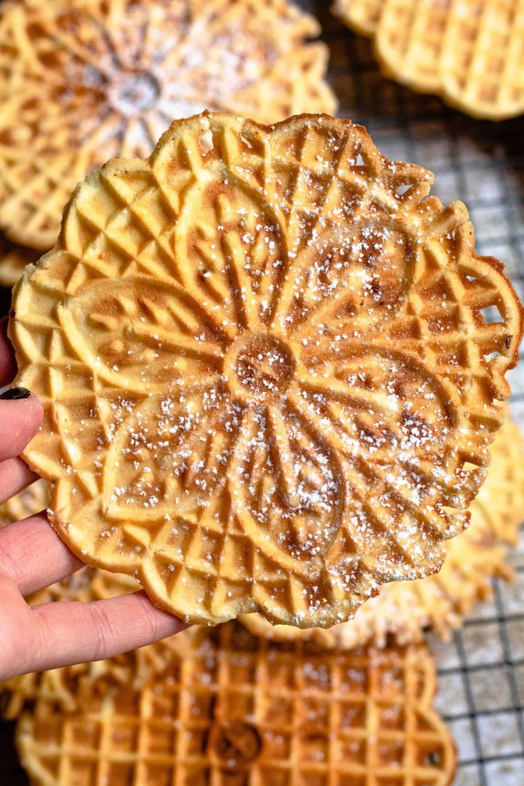 a hand holding up a waffle with powdered sugar on it in front of other waffles