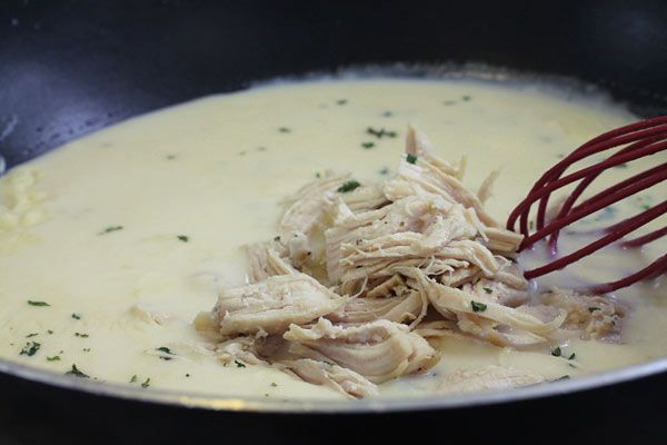 chicken and cream sauce in a pan with a red whisk