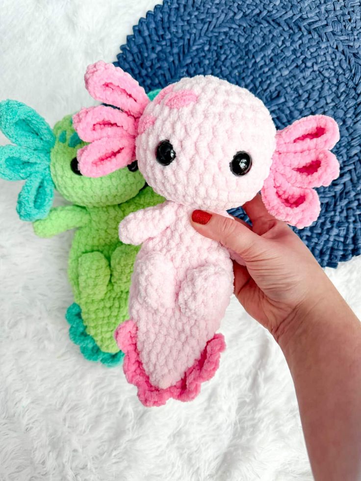 a hand holding a small crocheted stuffed animal next to two smaller knitted toys