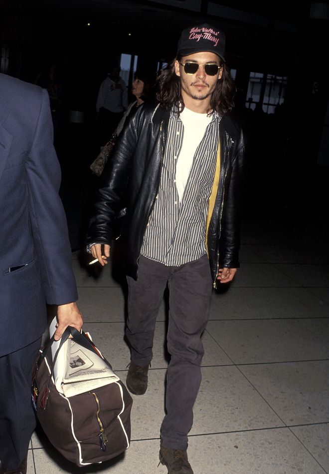 a man in a leather jacket carrying a duffel bag while walking through an airport