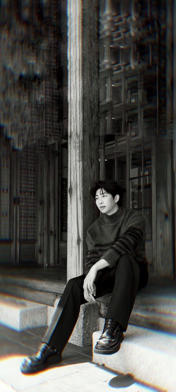 a young man sitting on top of a wooden bench next to a tall pole in front of a building