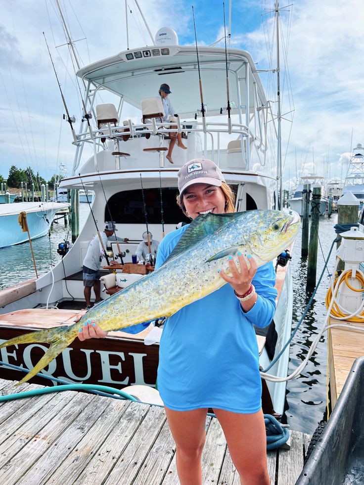 a woman holding a large fish while standing on a dock