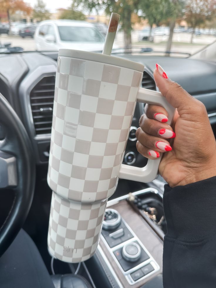 a woman holding a coffee cup in her hand while sitting in the driver's seat of a car