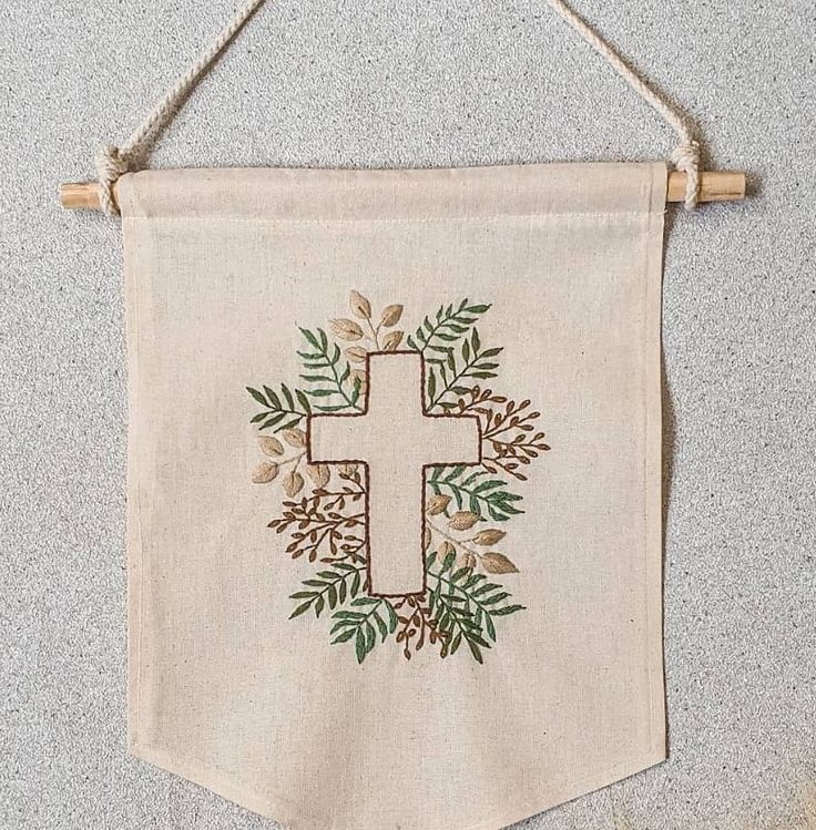 a wall hanging with a cross on it and some leaves around the edges, in front of a gray background