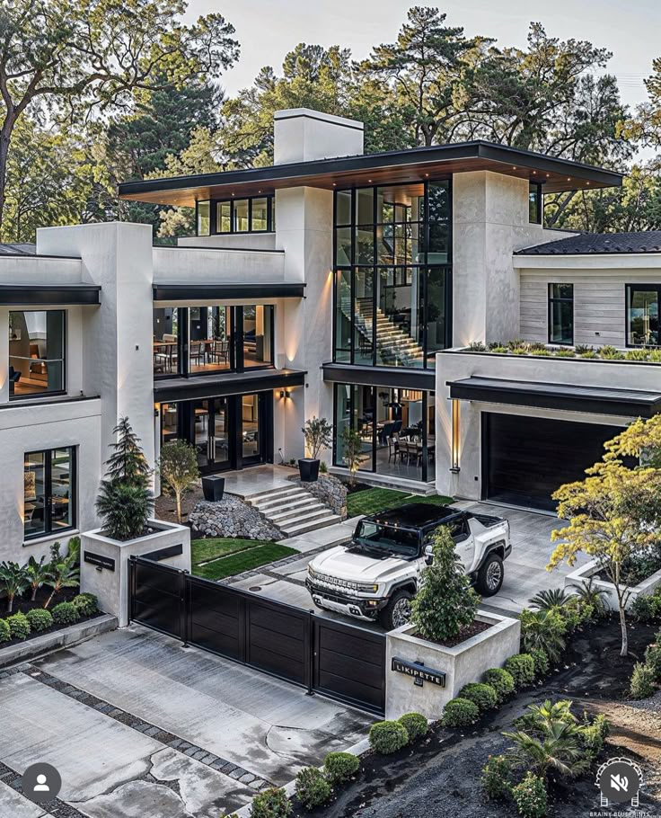 a modern house with two cars parked in the driveway and landscaping around it, surrounded by trees