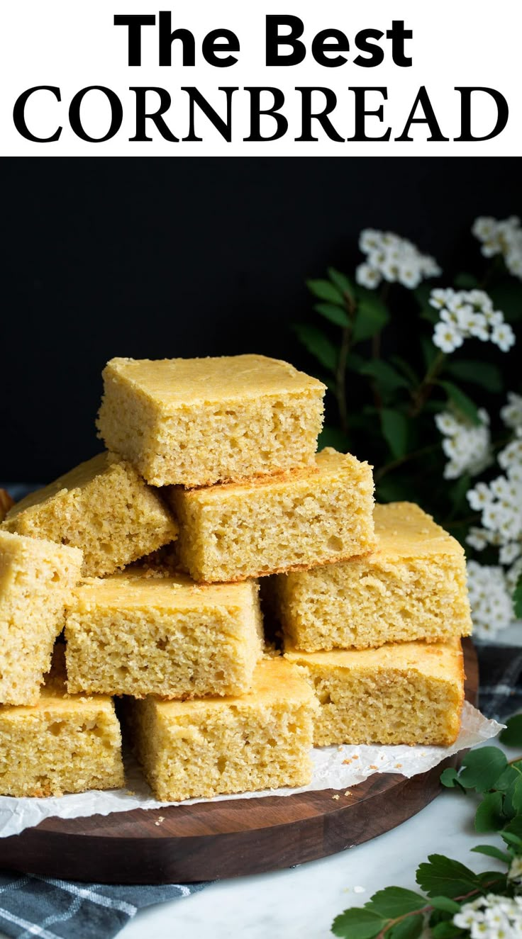 a pile of yellow cake sitting on top of a wooden cutting board next to flowers