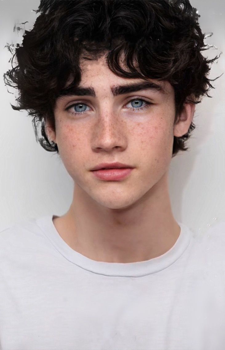 a young man with freckled hair and blue eyes looks at the camera while wearing a white t - shirt