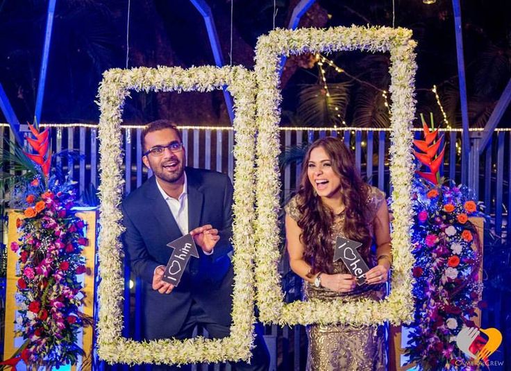 a man and woman standing in front of a photo booth with flowers on the wall