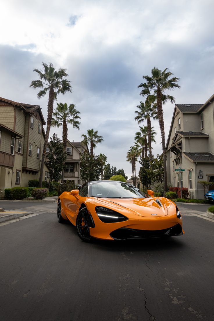 an orange sports car is driving down the street in front of palm trees and apartment buildings