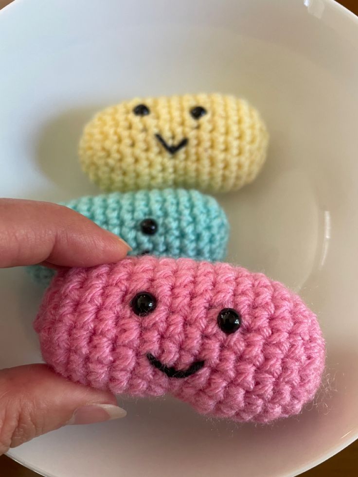 three crocheted items in the shape of smiley faces on a white plate with a person's hand