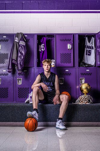 a man sitting on a bench in front of lockers with basketballs and jerseys