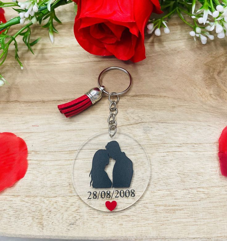 a keychain with a couple's silhouette on it and a red rose in the background