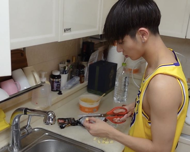 a young man in a yellow shirt is using scissors to cut up some food on the counter