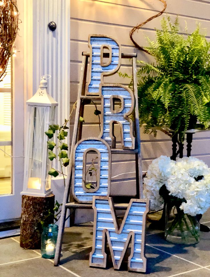 a wooden sign that says prom on the side of a house with flowers and greenery