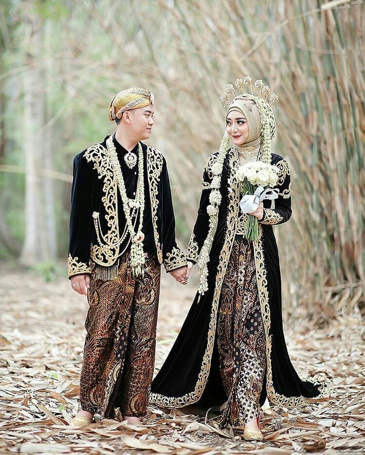 a man and woman dressed in traditional clothing walking through the woods holding hands with each other