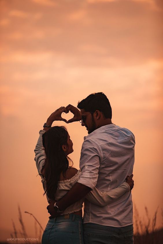 a man and woman standing next to each other with their hands in the shape of a heart