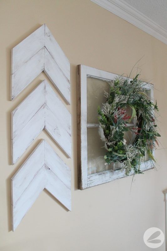 two wooden arrows hang on the wall next to a wreath and an old window frame