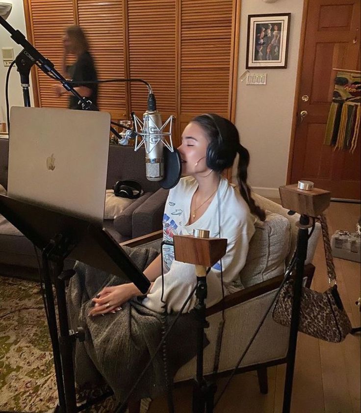 a woman sitting in a chair with a laptop on her lap, and a microphone behind her