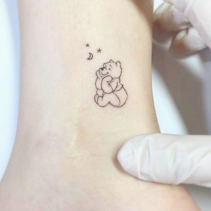 a small tattoo on the ankle of a person with a teddy bear holding a star