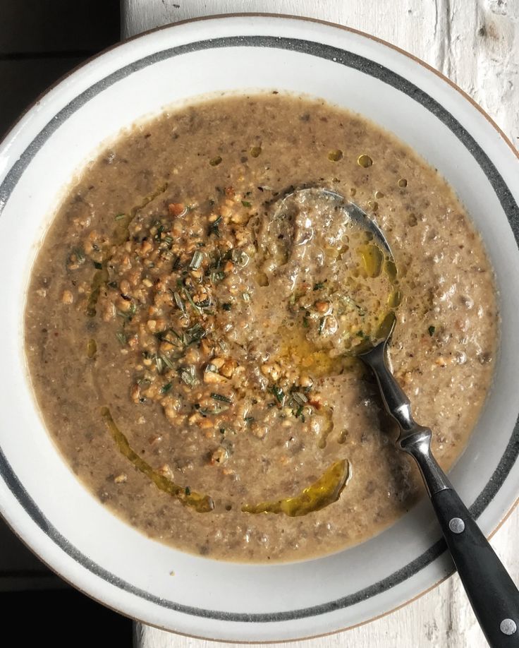 a white bowl filled with soup on top of a wooden table next to a spoon