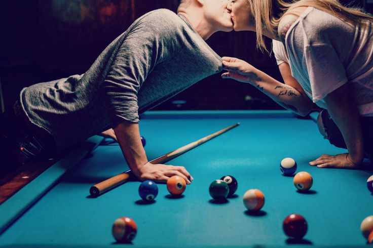 a man and woman kissing while playing pool