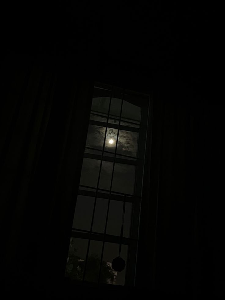 the moon is seen through a window at night