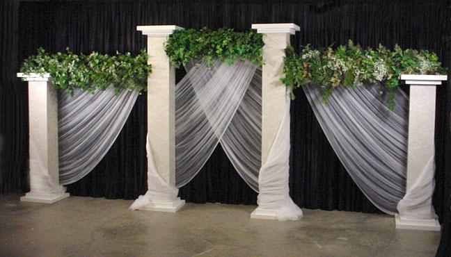 three white pillars decorated with greenery and sheer curtains